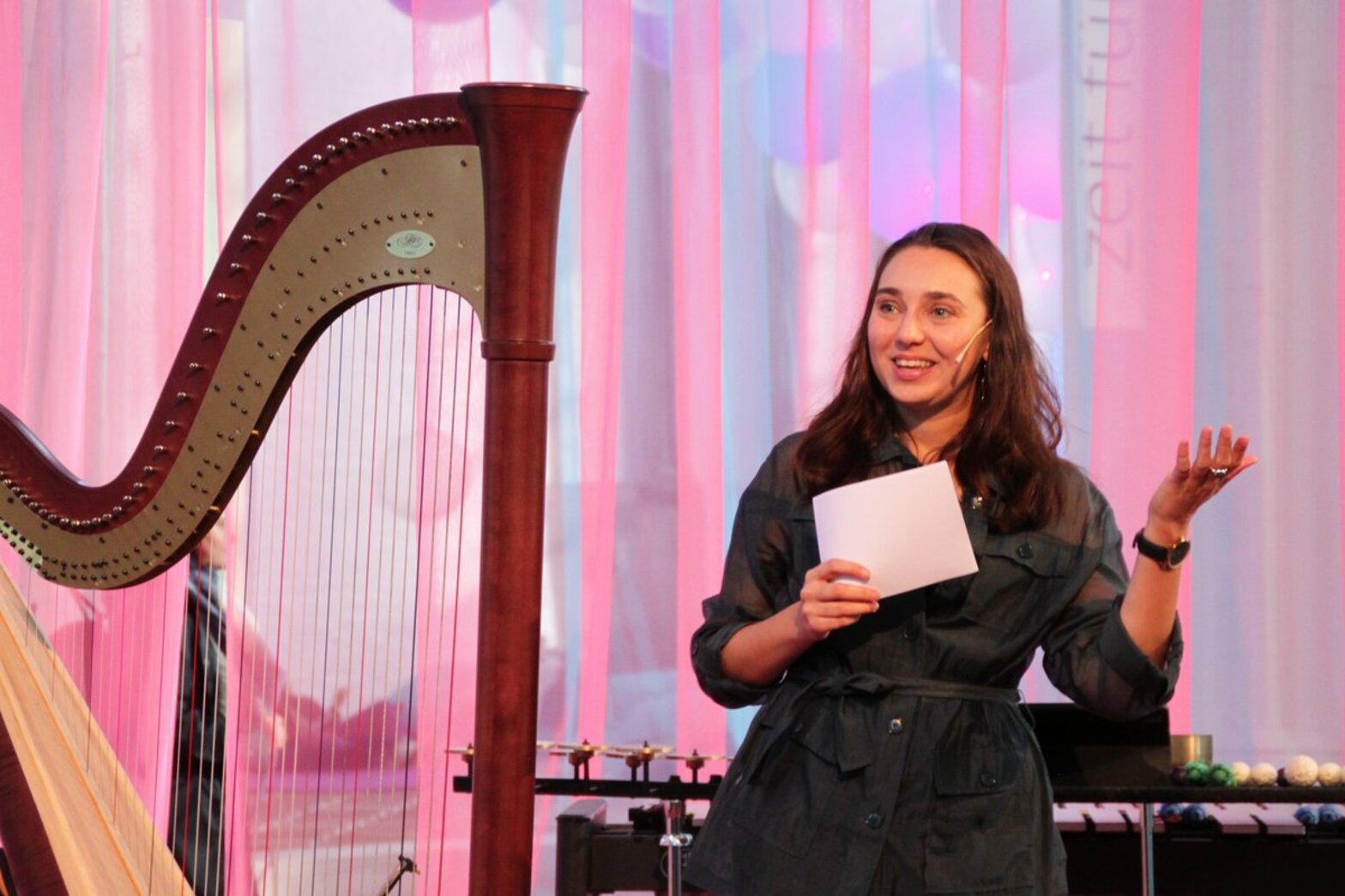 Eine Frau steht neben einer Harfe in einer Kirche und moderiert.