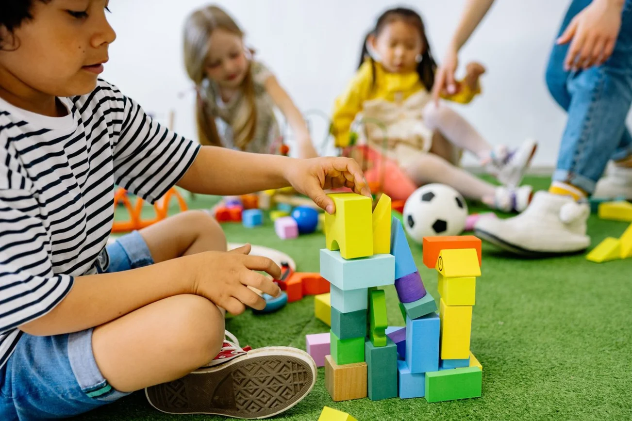 Kinder spielen mit Bauklötzen auf einem grünen teppich