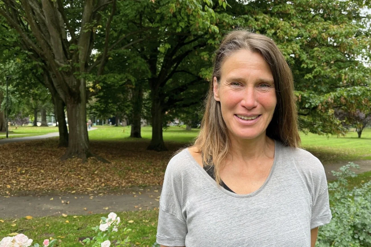 Eine Frau mit langen Haaren steht im Grünen und lächelt in die Kamera.