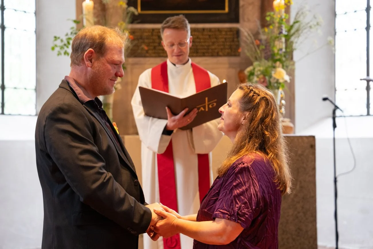 Ein Paar steht vor einem Pastor am Altar und schaut einander in die Augen. 