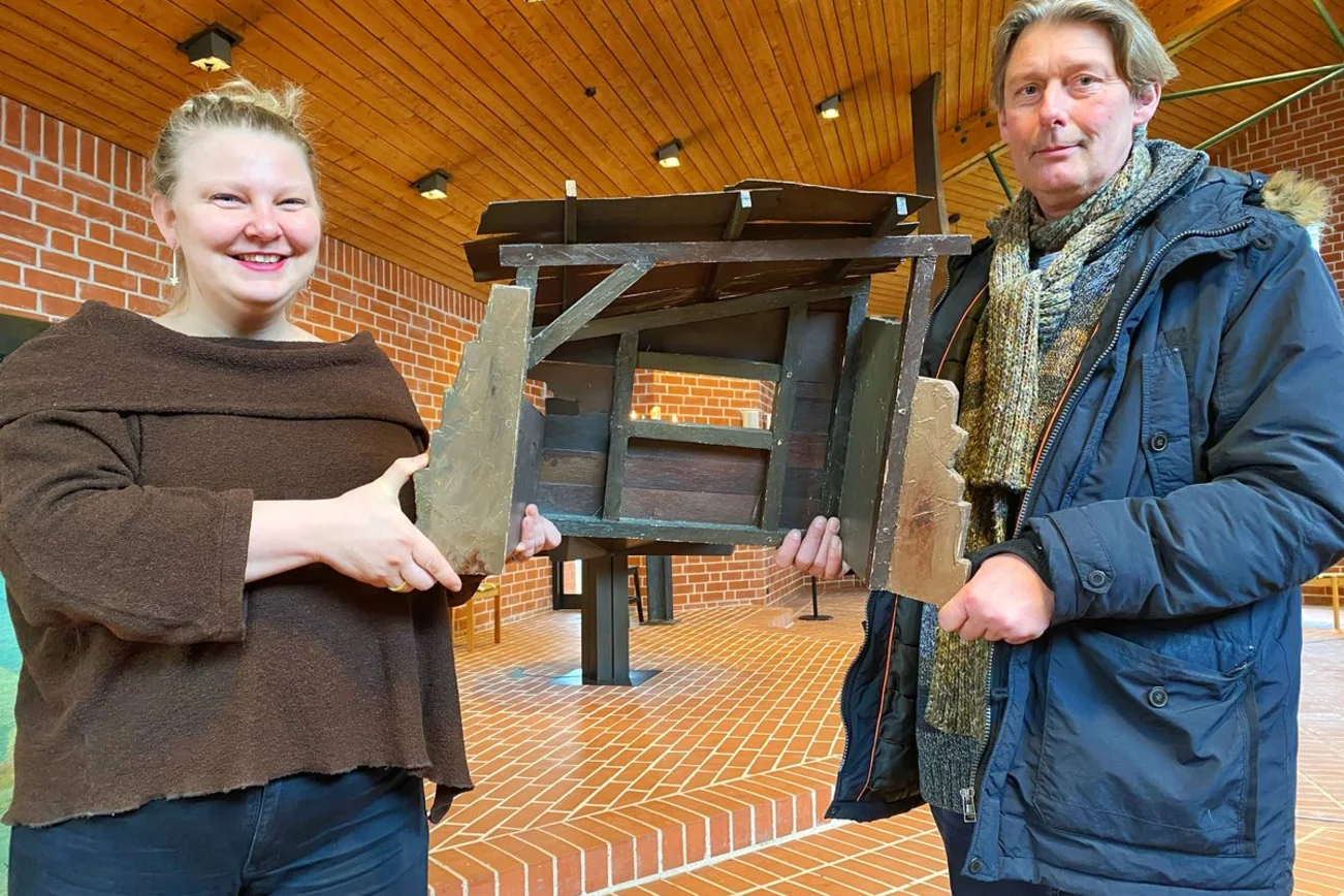Zwei Personen stehen in einer Kirche und halten eine Krippe in ihren Händen. 