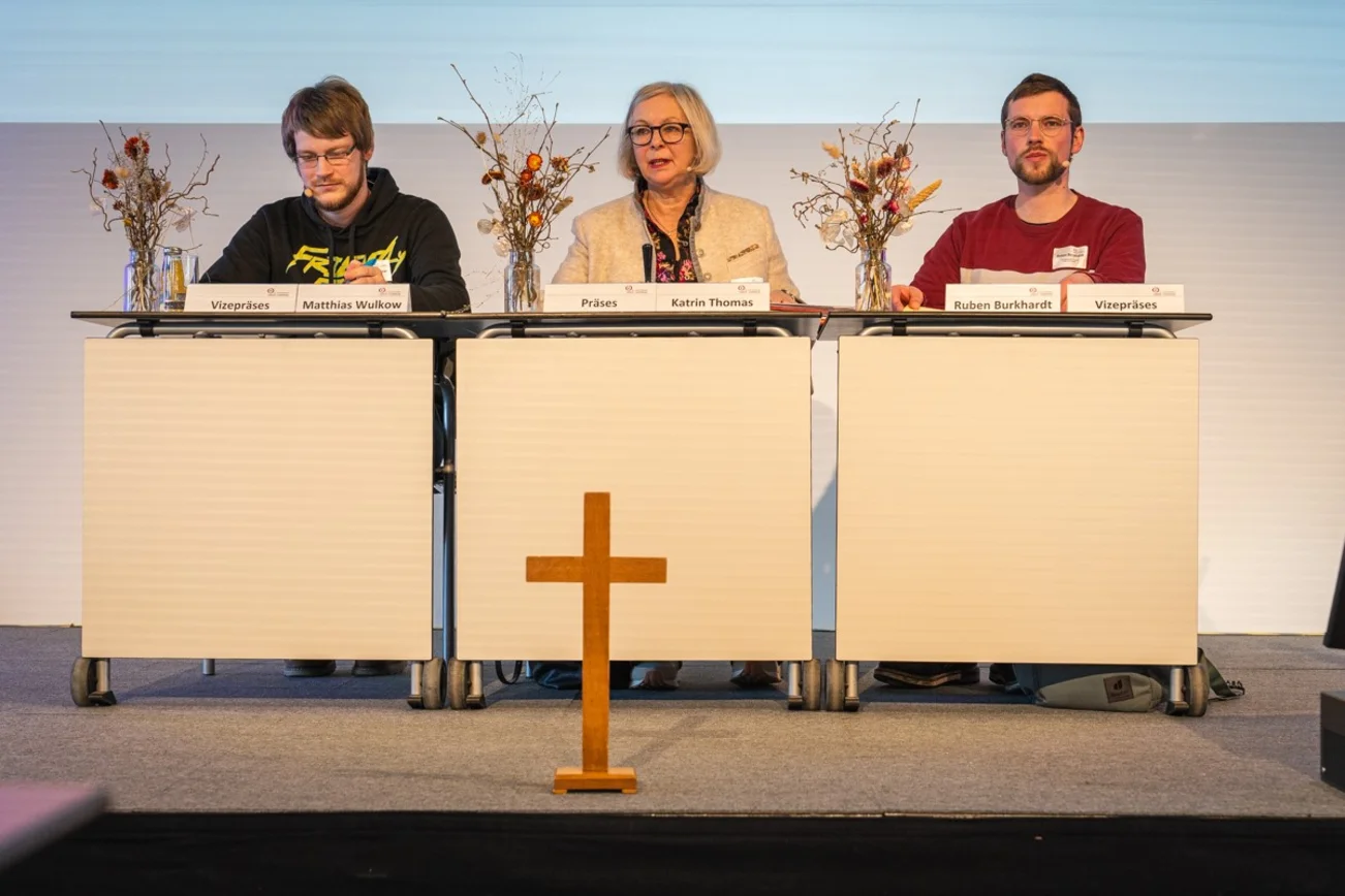 Das neue gewählte Synodenpräsidium aus drei Personen sitzt hinter einem großen Tisch.