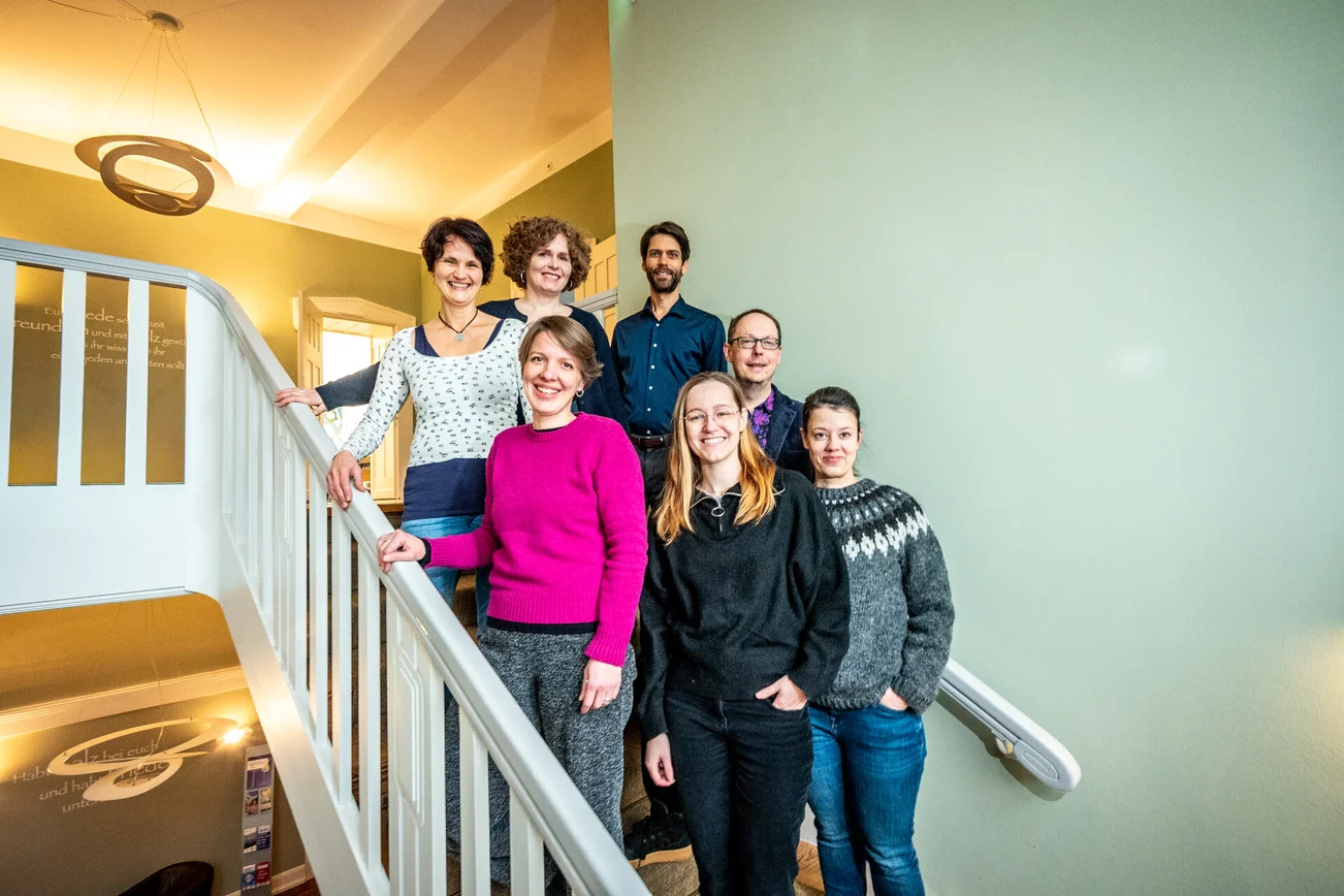 Eine Gruppe Menschen steht auf einer Treppe an einem weißen Treppengeländer.