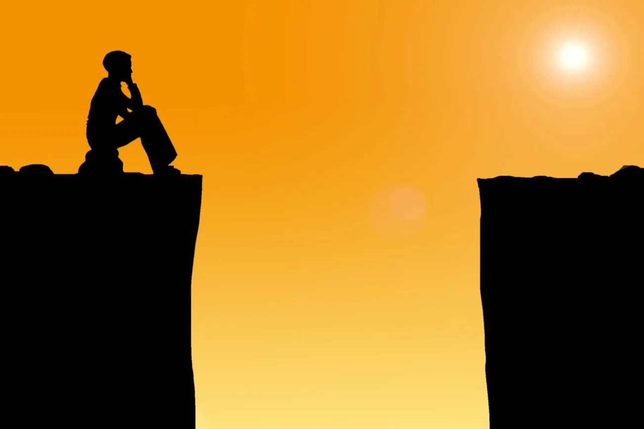 Eine Person sitz vor einer schwarzen Schlucht. Rechts im Bild scheint die Sonne durch einen orangefarbenen Hintergrund.