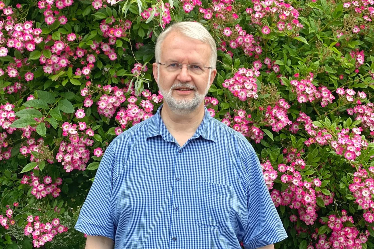 Ein Mann steht vor einer blühenden Hecke