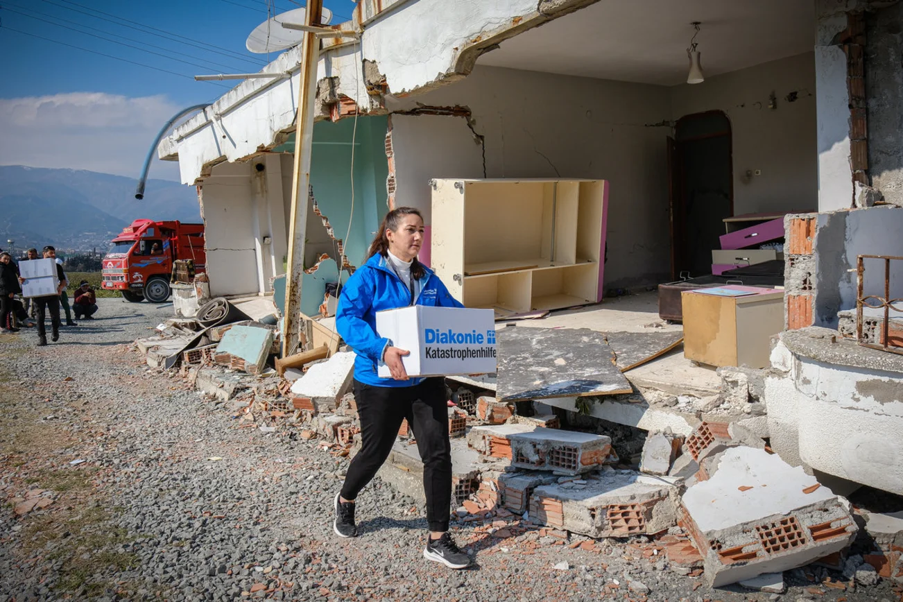 Eine Frau trägt einen Karton der Diakonie Katastrophenhilfe. 