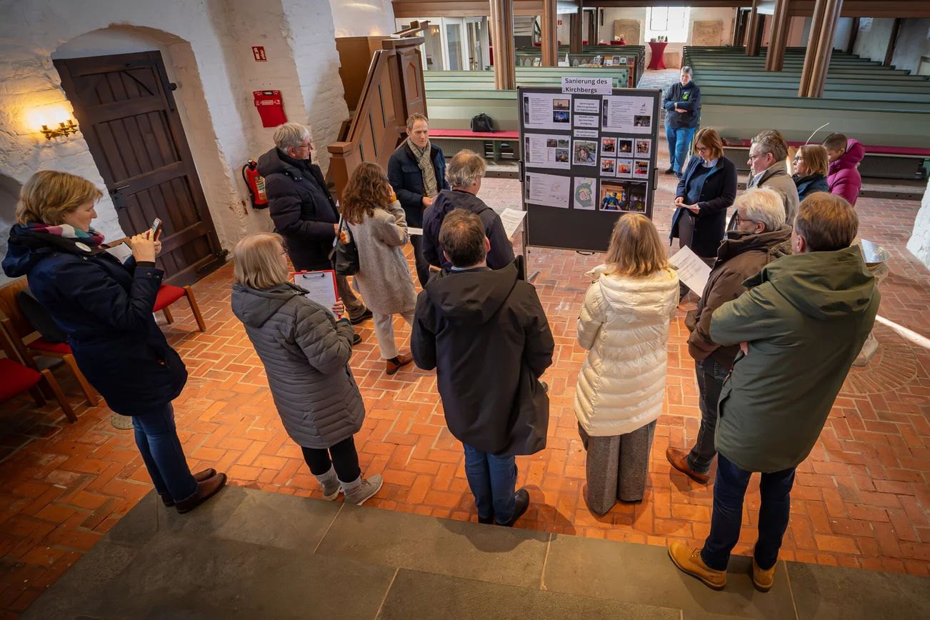 Mehrere Personen stehen in einer Kirche vor einer Stellwand mit Informationen und Fotos.