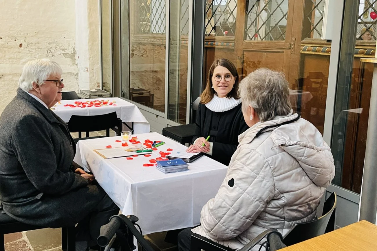Eine Pastorin spricht mit einem älteren Paar.