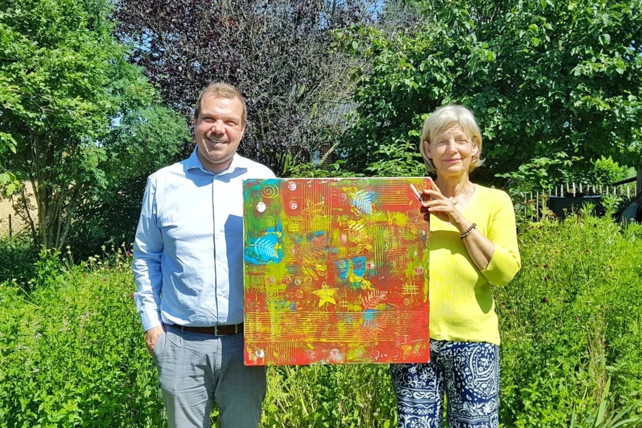 Zwei Menschen stehen in einem Garten und halten ein Bild fest. 