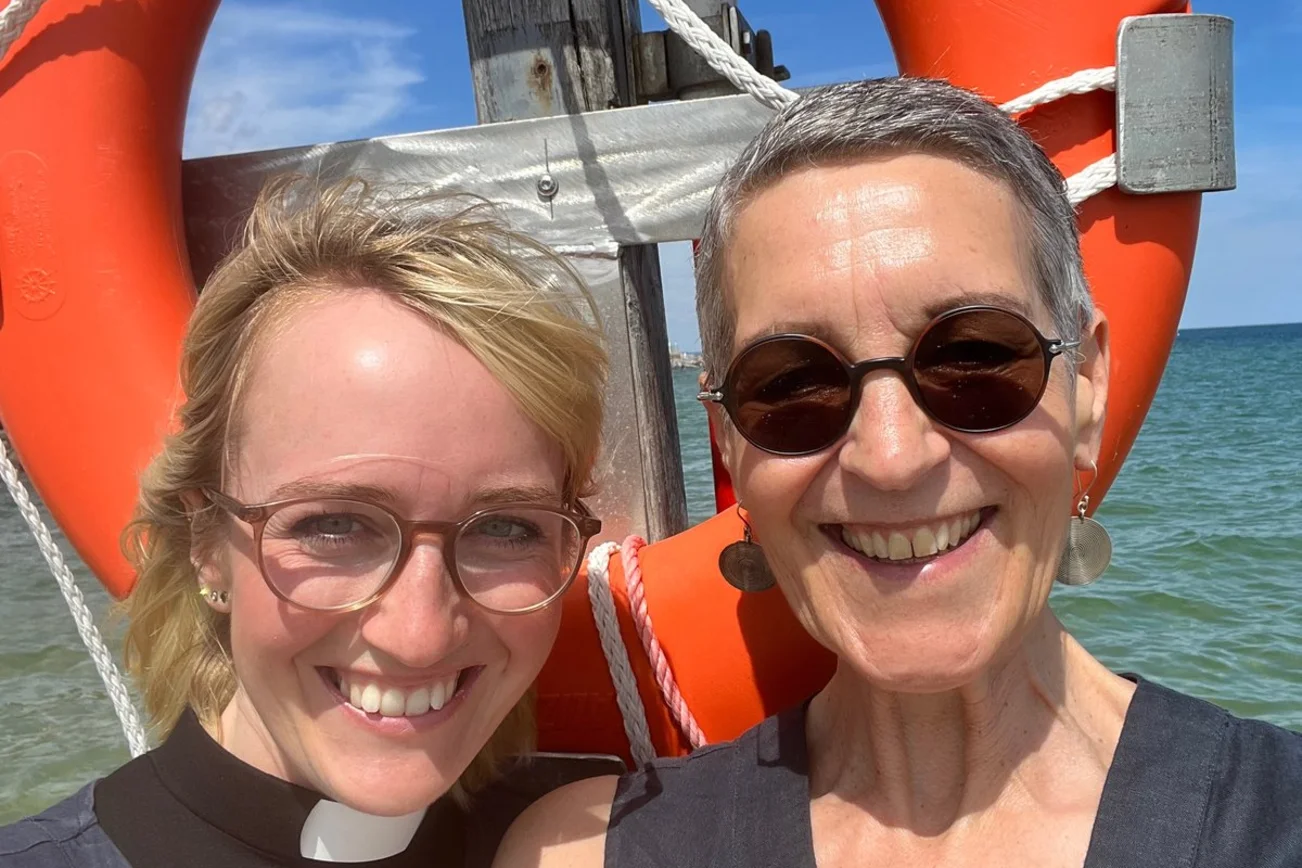 Zwei Personen stehend lächelnd am Meer. 