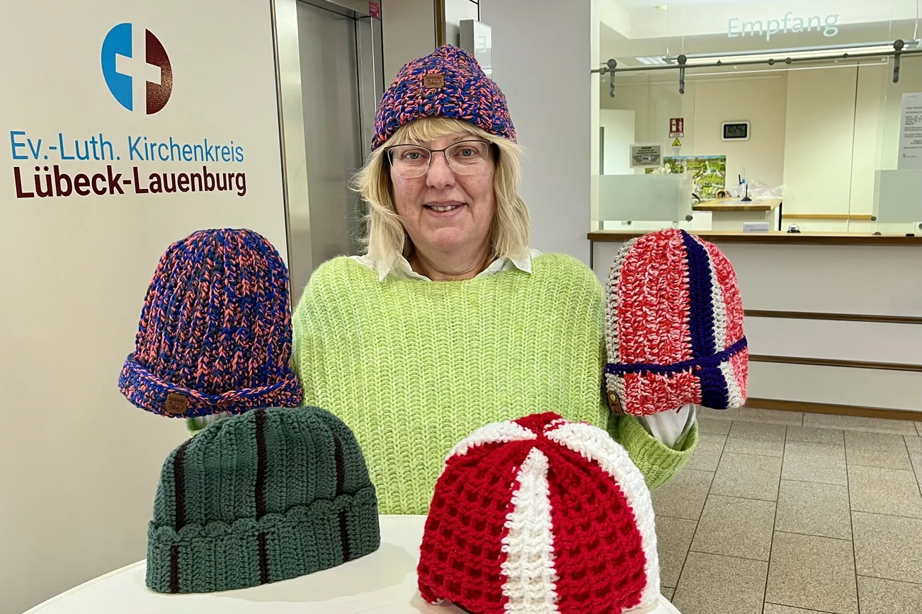 Eine Frau mit einer Mütze auf dem Kopf und Mützen auf dem Tisch davor.