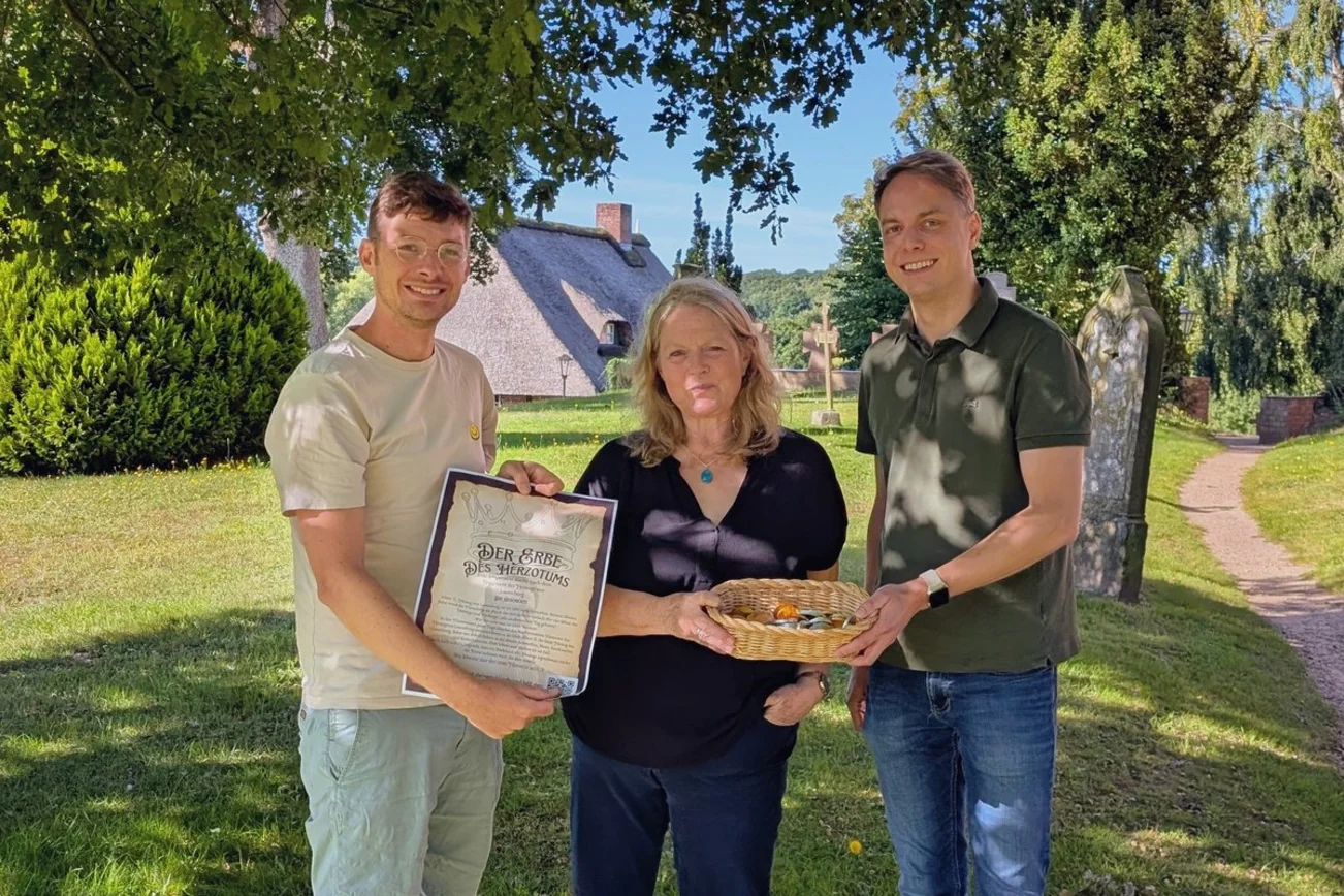 Drei Menschen stehen auf dem Berkenthiner Friedhof und schauen in die Kamera