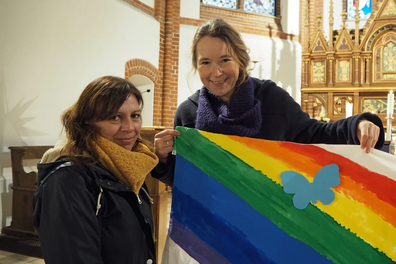 Zwei Frauen halten ein Banner mit einem Regenbogen