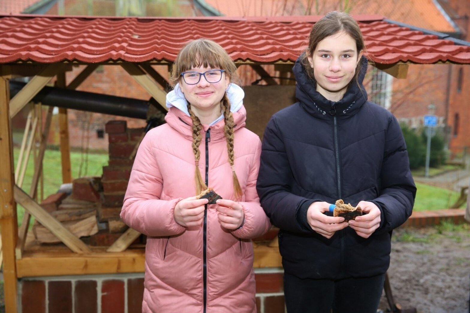 Zwei jugendliche Mädchen schauen mit einem gebackenen Brot in den Händen in die Kamera.