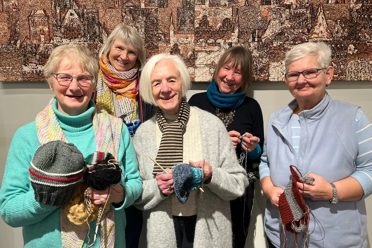 Fünf Frauen stehen mit Mützen und Strickzeug in den Händen im Foyer des Marienwerkhauses.
