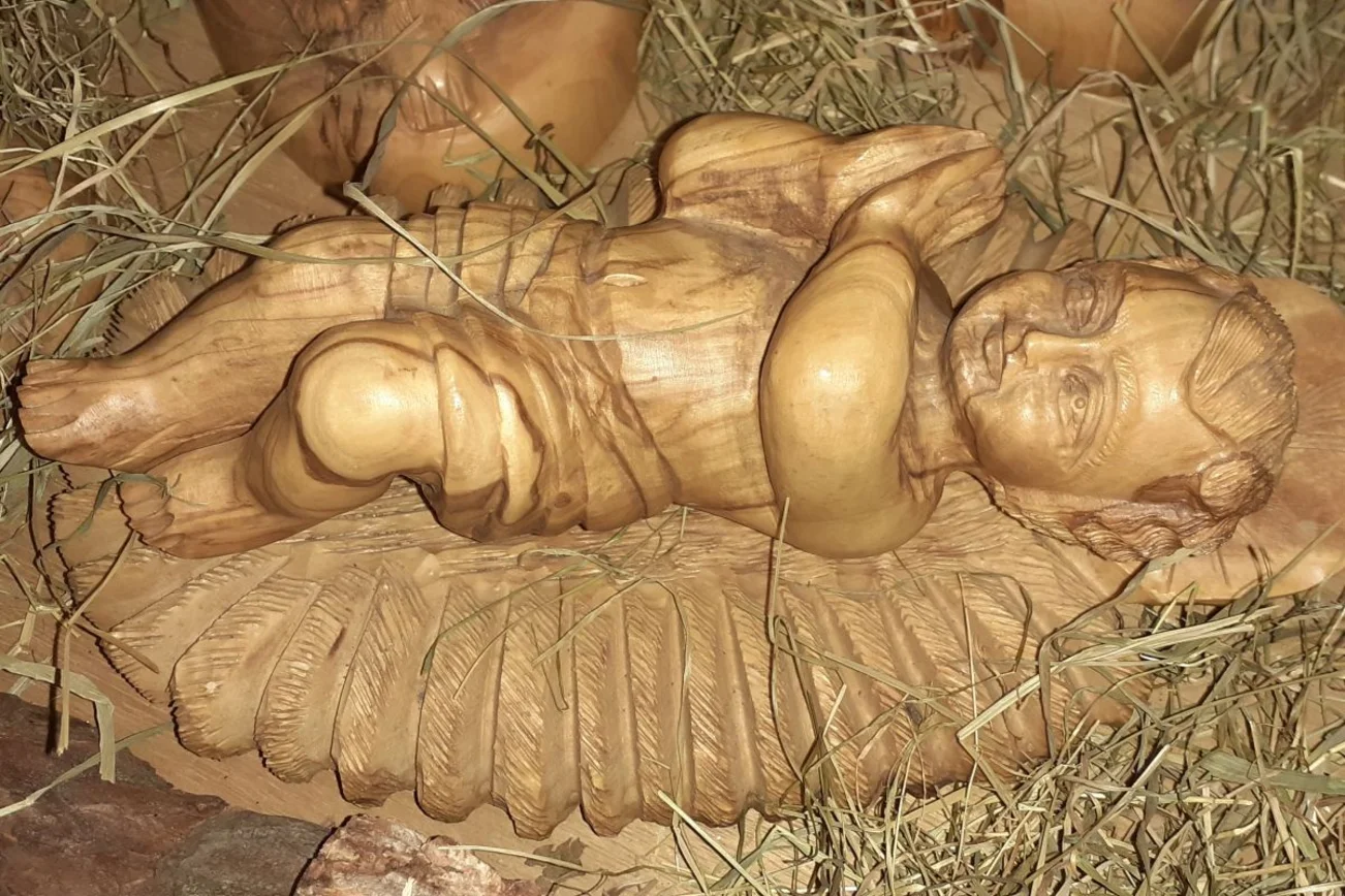 Das aus Holz geschnitzte Christuskind liegt mit betenden Händen in der Krippe