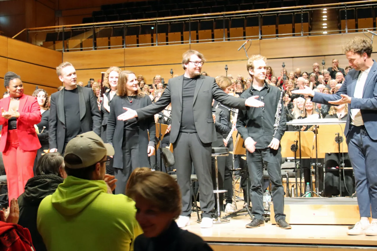 Mehrere Mitwirkende stehen am vorderen Rand einer Bühne und lächeln sich an. 