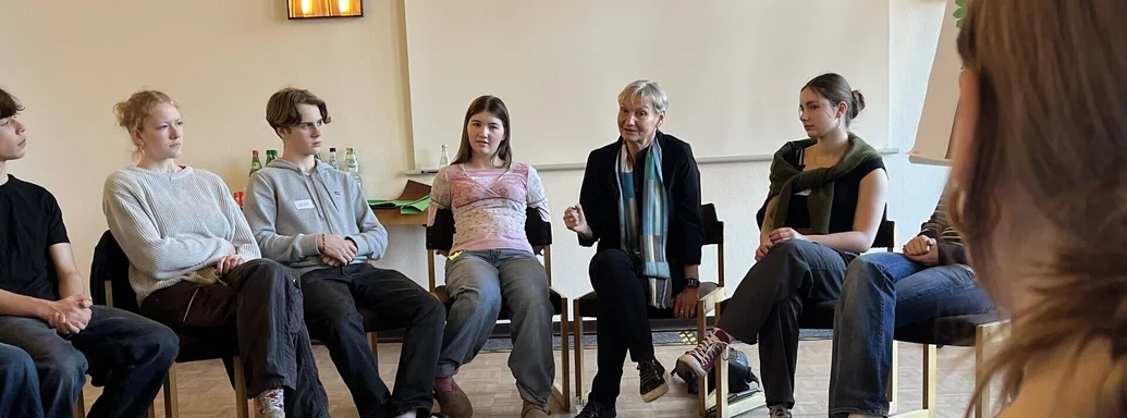 Junge Menschen und eine Frau sitzen im Kreis und wirken sehr konzentriert.