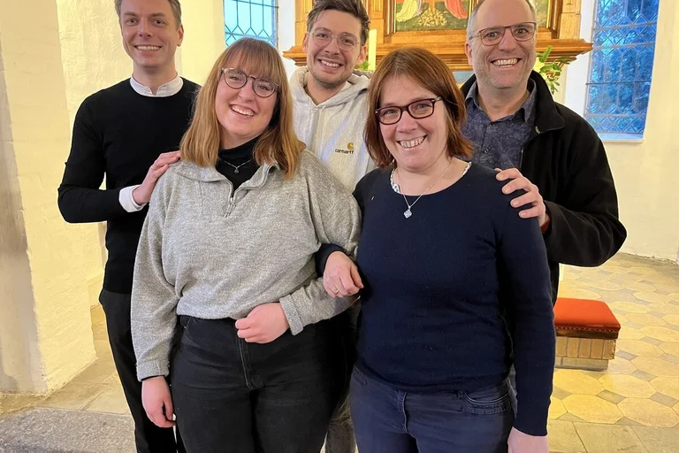 Fünf Personen stehen lächelnd in einer Kirche.