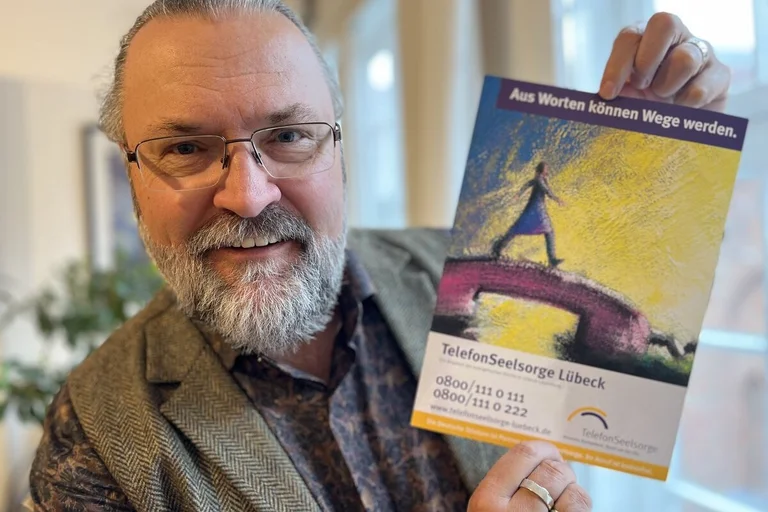 Ein Mann hält lächelnd ein Plakat in die Kamera. 