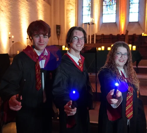 Drei junge Menschen in Verkleidung halten leuchtende Zauberstäbe.