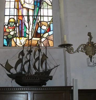 Blick auf ein Kirchenfenster und ein darunter stehendes Segelschiff-Modell