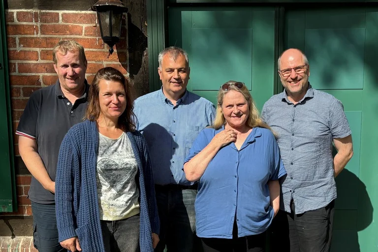 Drei Männer und zwei Frauen stehen vor einem Backstein-Gebäude.