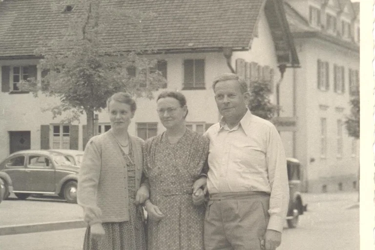 Ein historisches Foto. Drei Menschen sind zu sehen. Sie stehen eingeharkt nebeneinander.