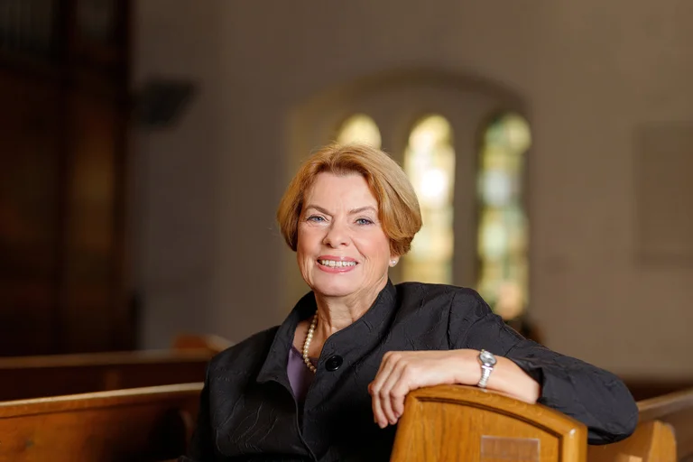 Eine Frau sitzt lächelnd in einer Kirche. 