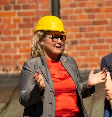 Eine Frau mit rotem Oberteil und gelbem Oberteil spricht vor einer Backsteinmauer