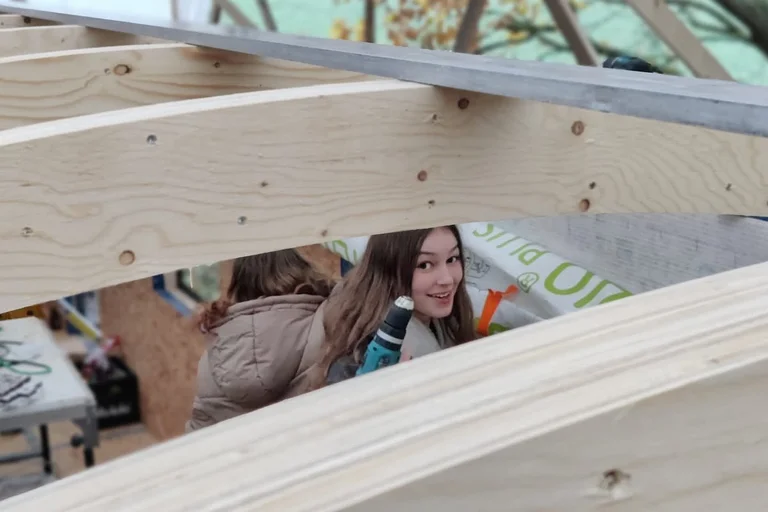 Eine junge Frau schaut zwischen den Deckenbalken eines Bauwagens hervor.