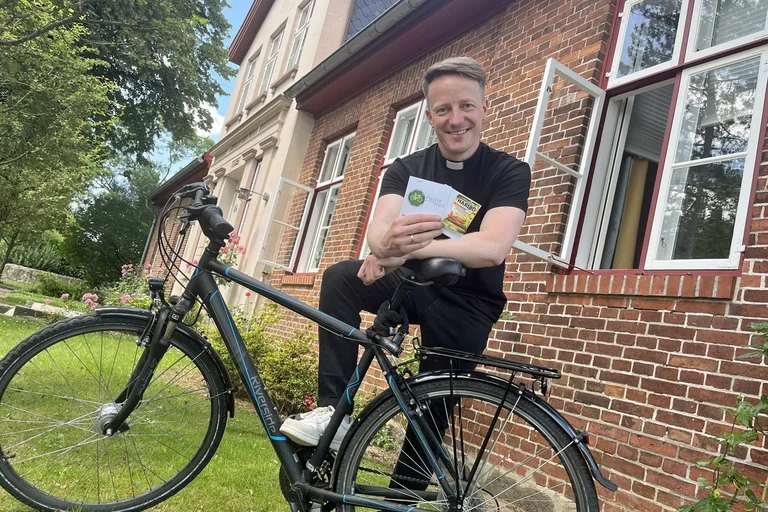 Ein Mann stützt sich auf ein Fahhrad, lächelt und hält zwei Karten in der Hand.