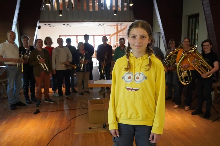 Ein Mädchen im Vordergrund, dahinter ein Posaunenchor in einer Kirche