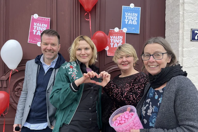 Ein Mann und drei Frauen stehen vor einer Kirchentür mit Plakaten zum Valentinstag.