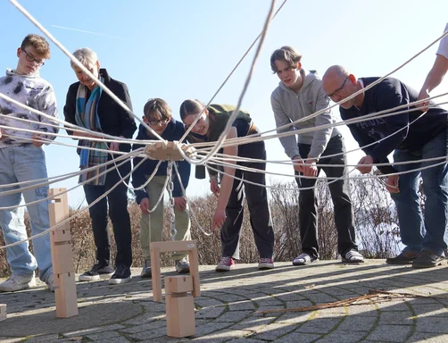 Menschen stehen im Kreis und halten Seile, die in der Mitte zusammenlaufen.