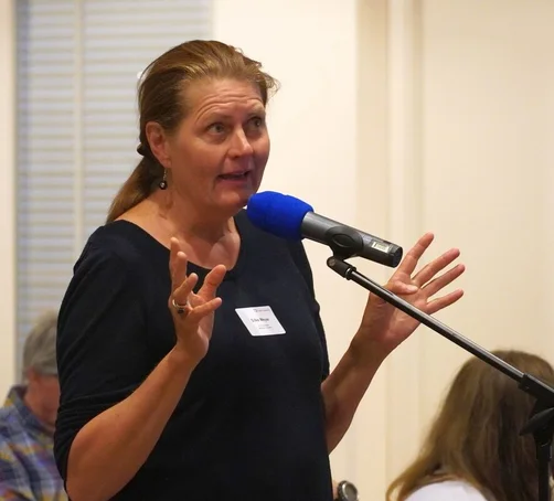 Eine Frau steht gestikulierend an einem Mikrofon. 