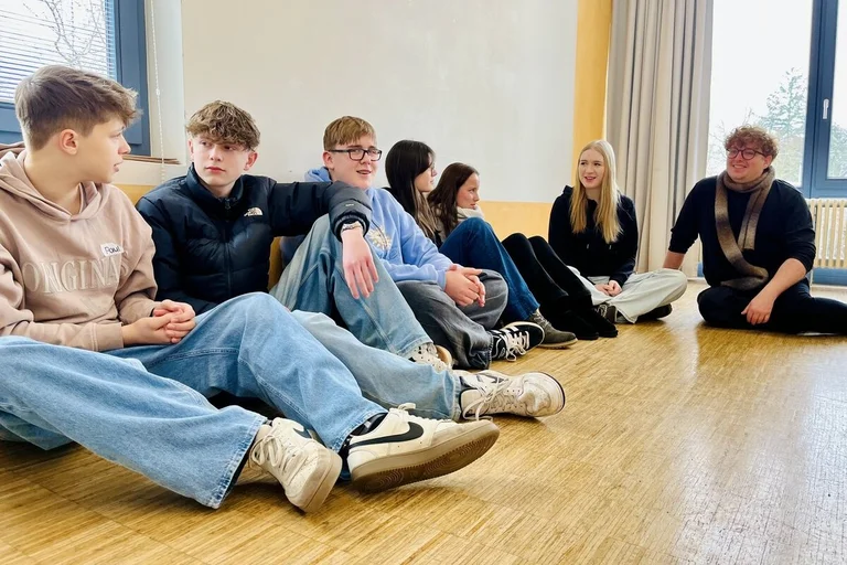 Jugendliche und der Pastor sitzen auf dem Boden und unterhalten sich