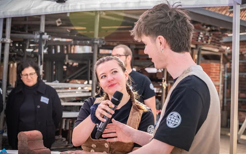 Eine junge Frau in Handwerkerkluft interviewt einen jungen Mann.