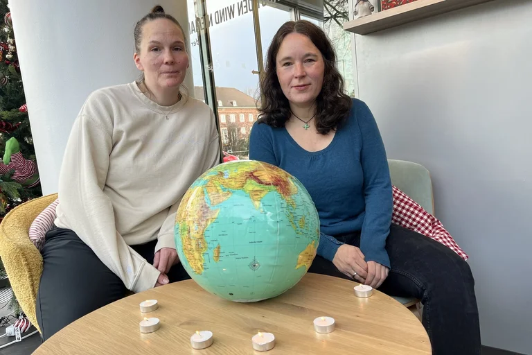 Zwei Frauen sitzen an einem Tisch, auf dem ein Globus Ball liegt. Darum stehen Teelichter.