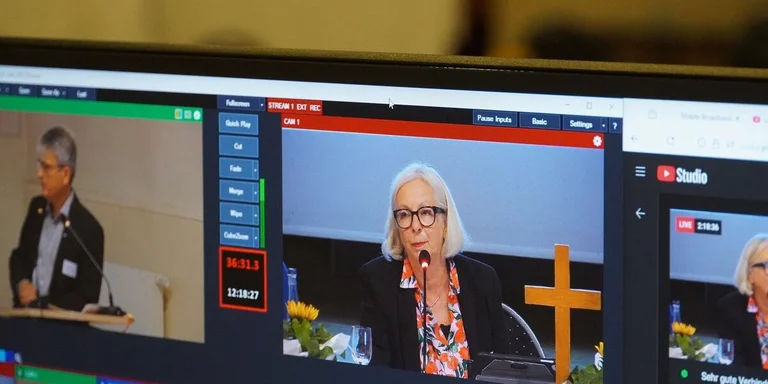 Ein Bildschirm der eine Frau zeigt, die an einem Mikrofon sitzt.