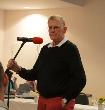 Ein Mann mit grauen Haaren steht an einem Mikrofon