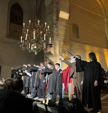 Eine große Gruppe Darsteller steht am Rand einer Bühne und hält Zauberstäbe in die Luft.