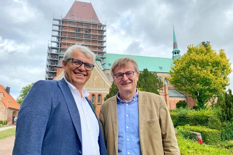 Zwei Männer stehen lächelnd vor einer Kirche
