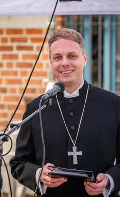 Ein Mann in schwarzem Pastorengewand spricht an einem Mikrofon