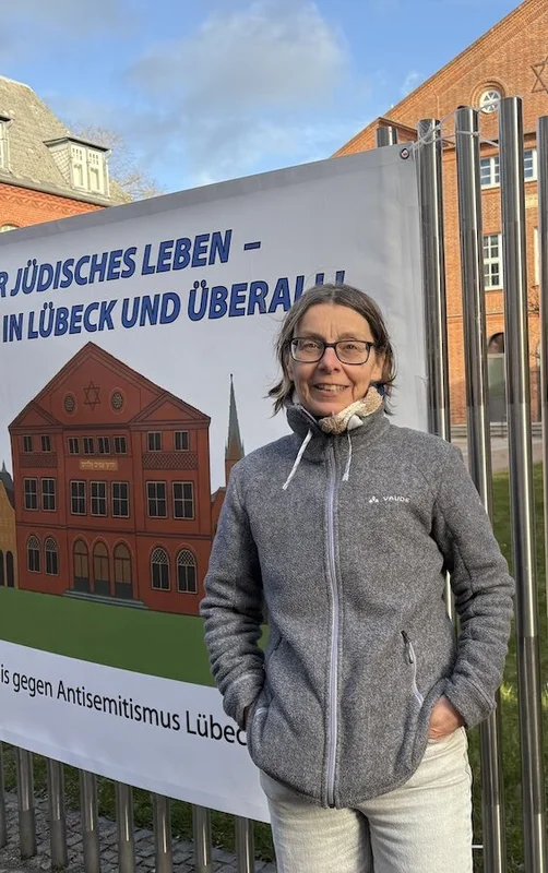 Eine Frau steht vor einem Zaun mit einem Banner an der Lübecker Synagoge