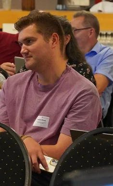 Drei Personen sitzen in einer Stuhlreihe und hören zu. 