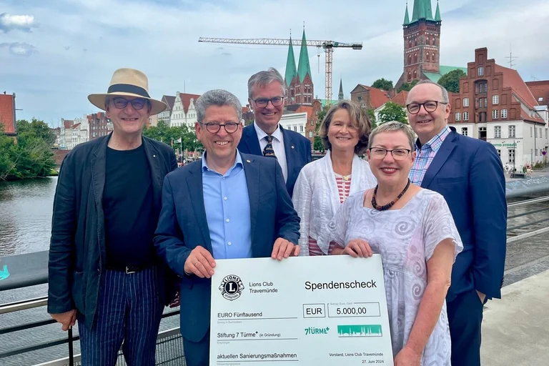 Sechs Menschen halten einen Check in den Händen und lächeln in die Kamera.