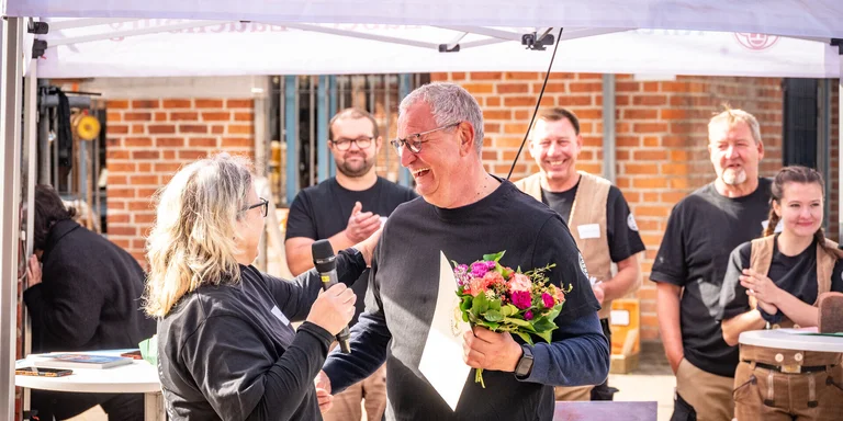 Eine Frau übergibt einen Blumenstrauß an einen Mann. Beide lachen. 