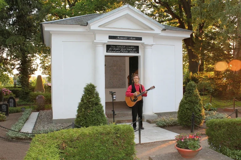 Ein Mann steht mit seiner Gitarre vor einem Grabmal.