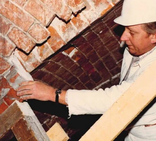 Ein Bararbeiter mit Bauhelm nimmt einen Backstein aus der Backstein-Wand.